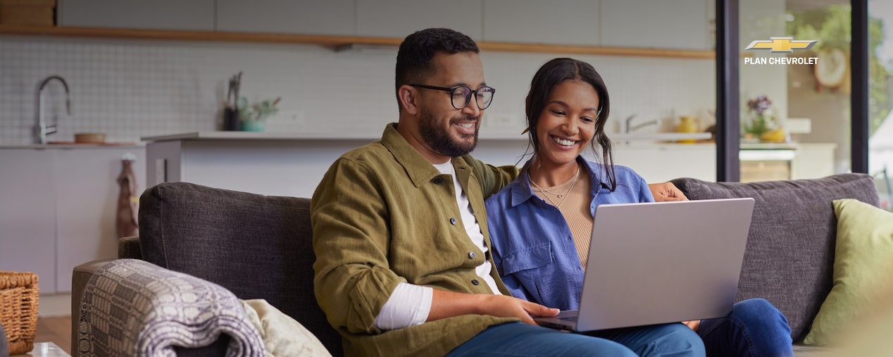 Personas sentadas en un sillón usando una notebook con mensaje de suscripción digital para comprar un 0 km de Chevrolet de forma fácil y segura