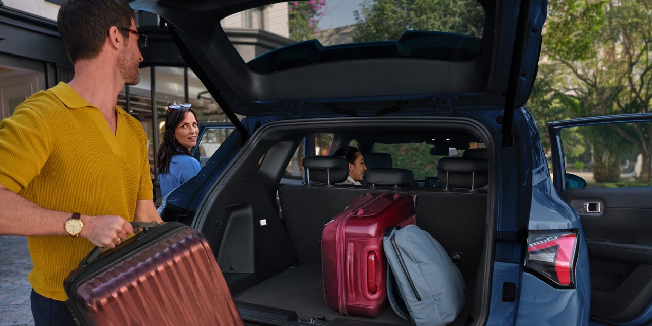 Chevrolet Captiva Híbrida azul con apertura eléctrica del baúl y capacidad de carga para equipaje. Dos maletas, una mochila y tres personas preparándose para un viaje en un entorno residencial.