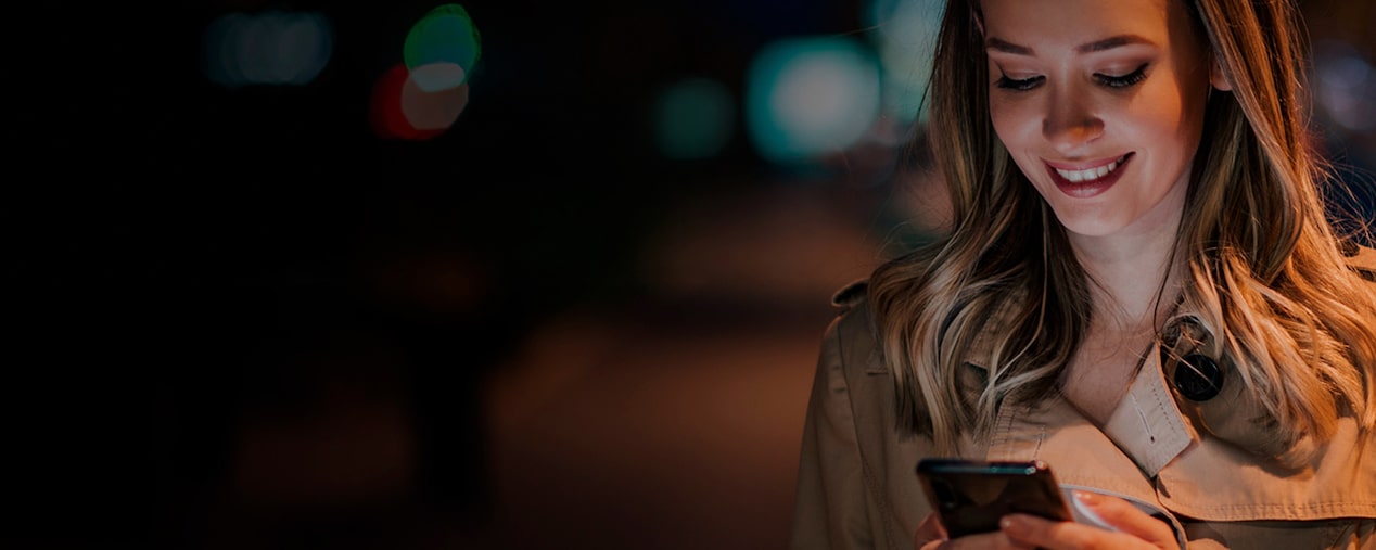Persona mirando un smartphone y sonriendo en un entorno urbano nocturno, imagen que acompaña la sección 'Cobrar Haber Neto' dedicada a explicar el proceso de cobro digital de suscripciones Chevrolet.