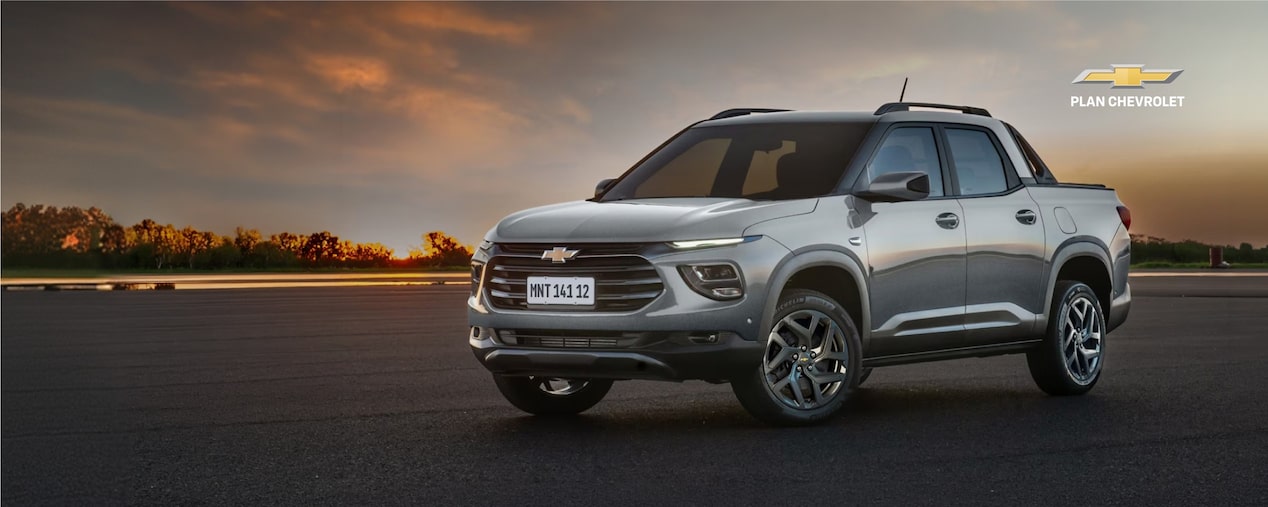 Chevrolet Montana LT AT gris estacionada sobre una pista al atardecer, con el cielo iluminado por la puesta de sol al fondo. Imagen promocional de Plan Chevrolet con oferta de financiación de hasta 80% en 120 cuotas y seguro bonificado al 50% durante los primeros 3 meses.