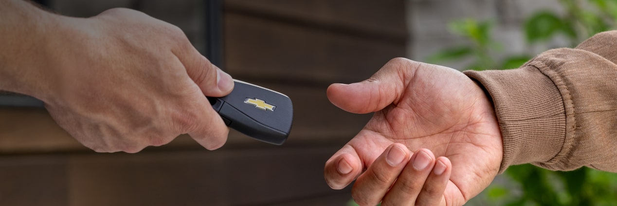 Dos manos entregando una llave con logo Chevrolet, bajo el título 'Resultados y Participación', imagen que representa la participación de clientes en programas de adjudicación y resultados de la suscripción digital Chevrolet.