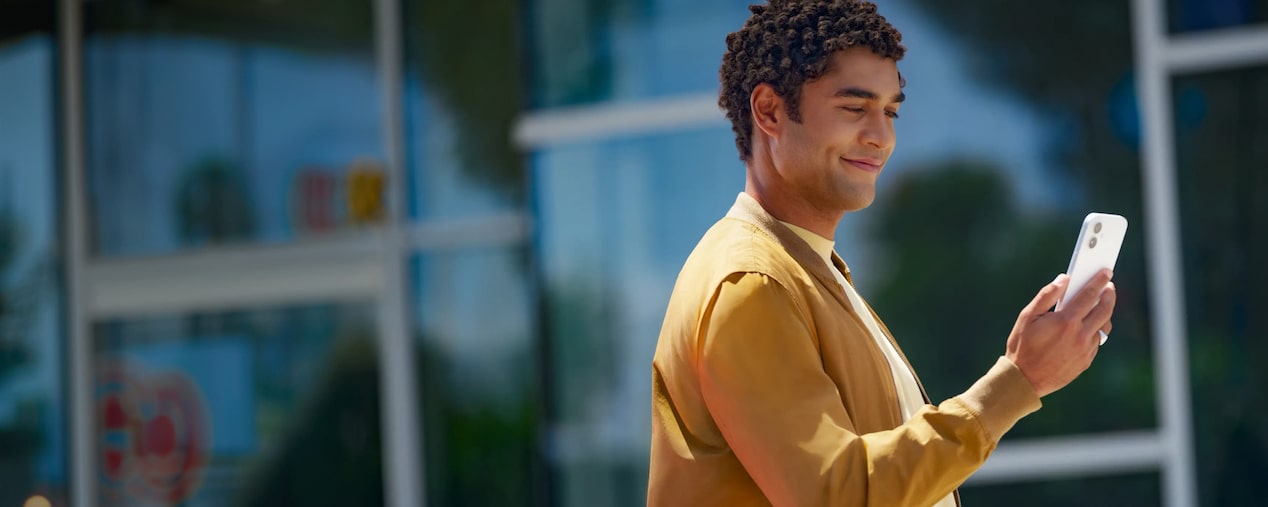 Persona al aire libre mirando un smartphone con gesto sonriente, junto al título 'Últimas Novedades', imagen que representa el acceso móvil a respuestas y actualizaciones dentro de la página Últimas Novedades de la suscripción digital Chevrolet.