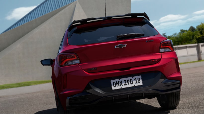 Vista en ángulo de tres cuartos frontal del nuevo auto Chevrolet Onix Hatchback RS 2027 color rojo en movimiento, destacando su exclusiva parrilla tipo panal y detalles oscurecidos en Argentina.