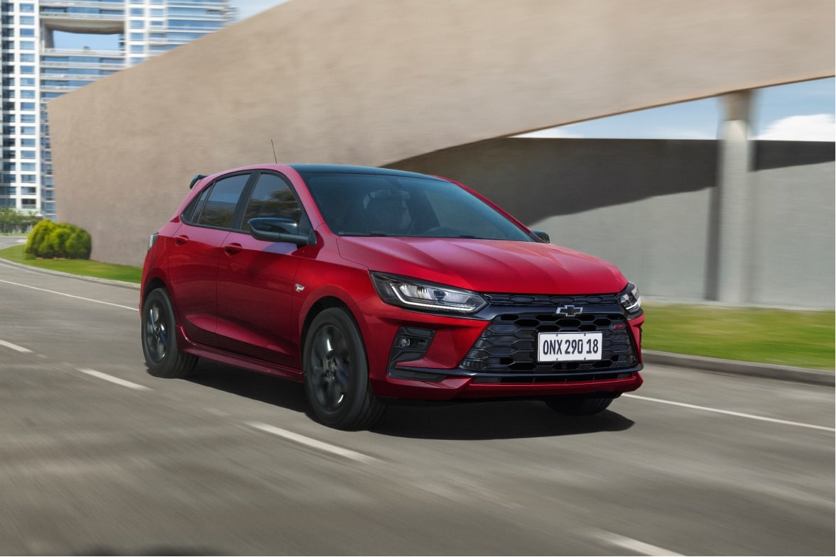 Vista exterior frontal en movimiento del nuevo auto Chevrolet Onix Hatchback RS 2027 color rojo circulando por la calle, demostrando su performance ágil y estética deportiva en Argentina.
