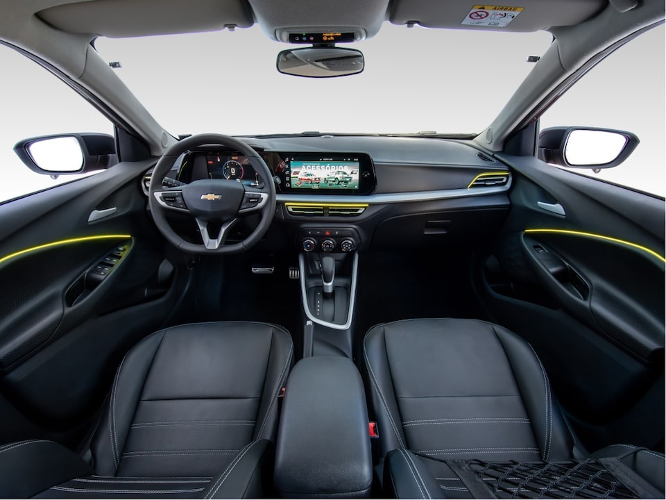 Vista interior y delantera del Chevrolet Onix Plus, mostrando volante, pantalla digital central, controles, guantera y más.