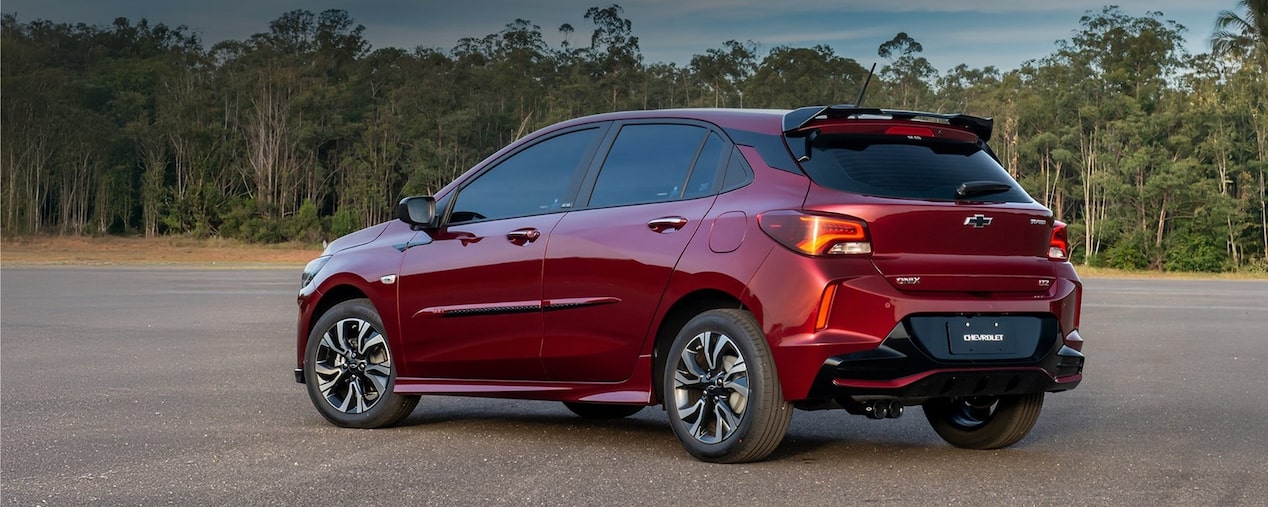 Vista lateral del Chevrolet Onix estacionado con vegetación de fondo.