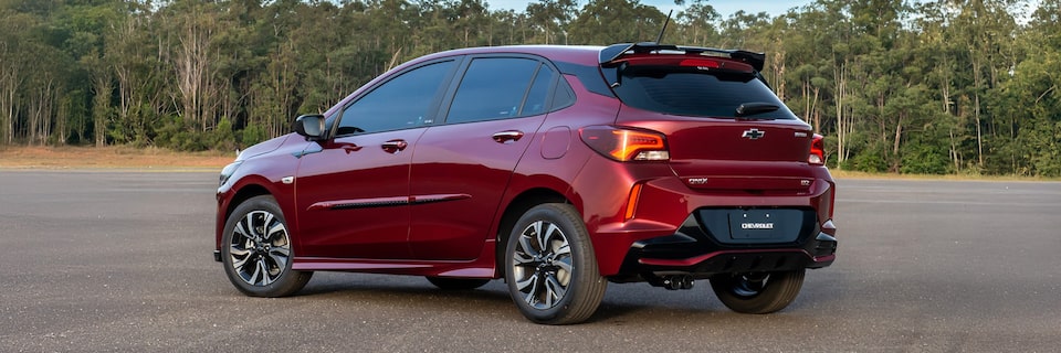 Vista lateral del Chevrolet Onix estacionado con vegetación de fondo.