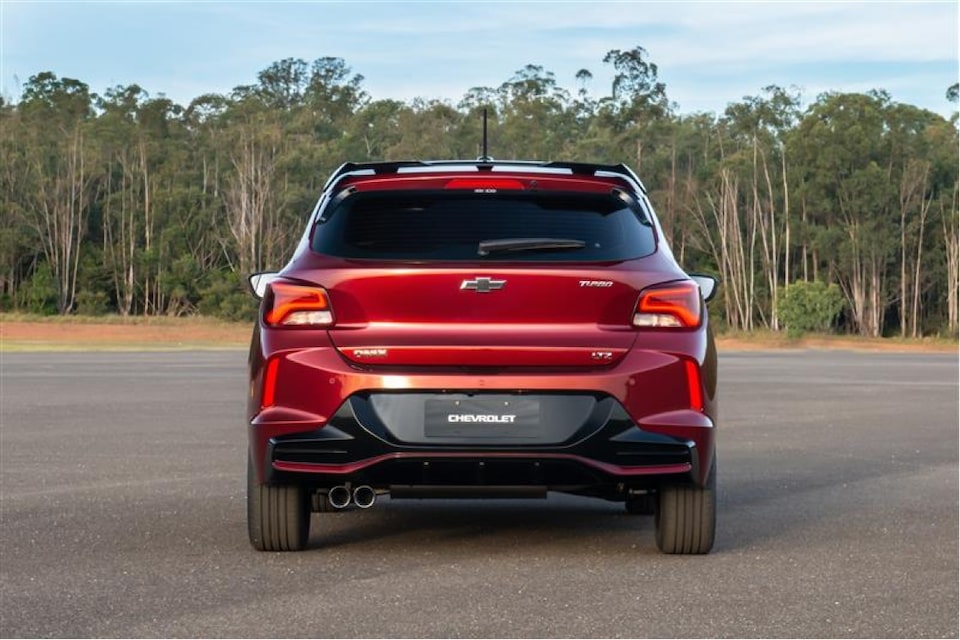 Vista trasera del Chevrolet Onix estacionado con vegetación de fondo.
