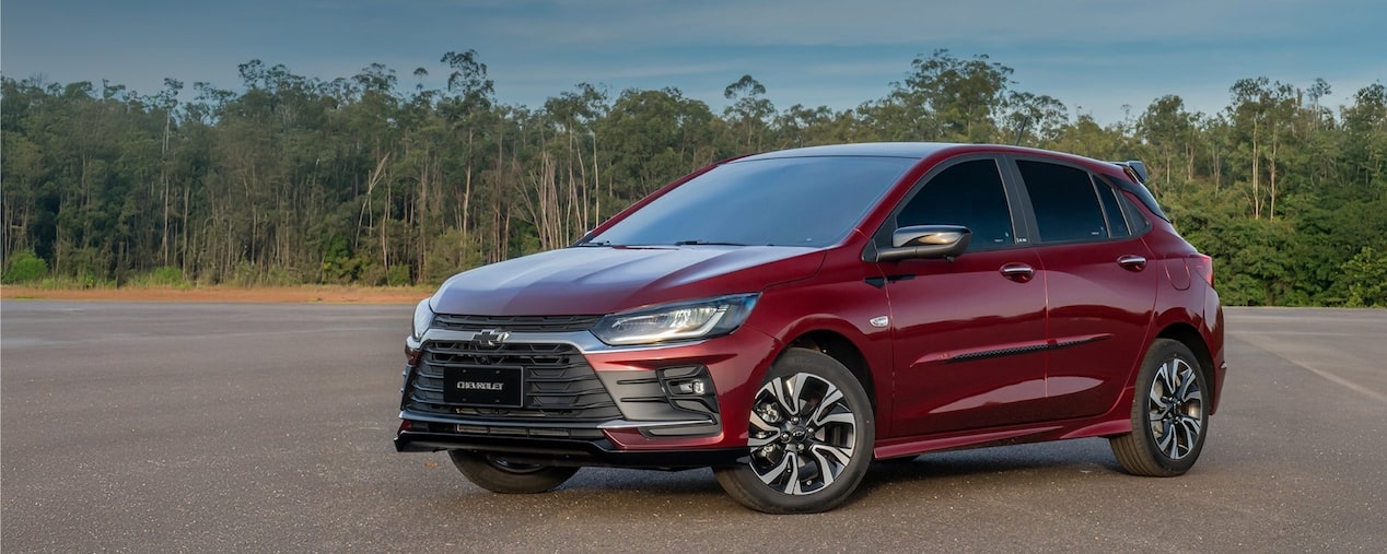 Chevrolet Onix estacionado con vegetación de fondo.
