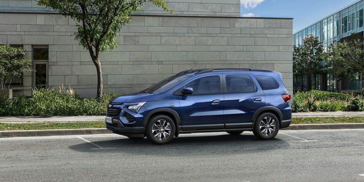 Chevrolet Spin 2027 azul estacionada en perfil lateral en entorno urbano moderno, destacando su equipamiento de seguridad activa y pasiva en Argentina.