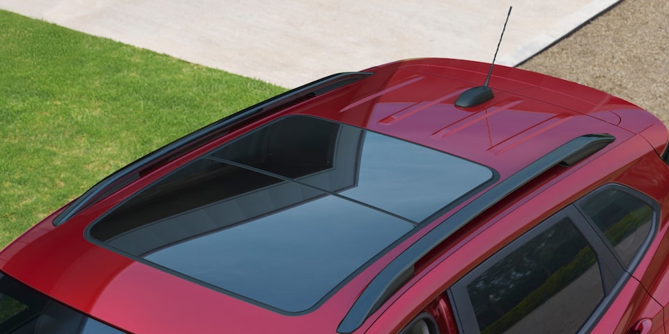 Vista superior de Chevrolet Tracker rojo, destacando su techo solar panorámico de vidrio y las barras longitudinales del techo.