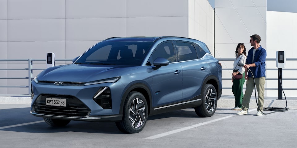 Imagen de un hombre y una mujer a punto de cargar una Chevrolet Captiva PHEV estacionada en una playa de estacionamiento con cargadores eléctricos.