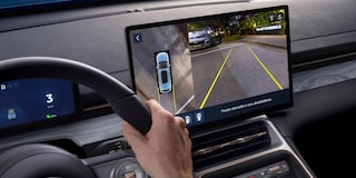 Imagen desde el punto de vista del conductor mientras observa la pantalla central digital y estaciona con la asistencia de la cámara trasera.