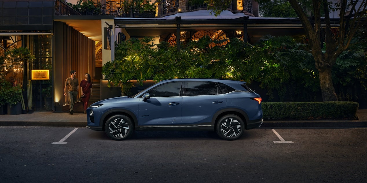Vista lateral de la Chevrolet Captiva PHEV estacionada en la puerta de un restaurante, mientras un hombre y una mujer salen por la puerta del local.