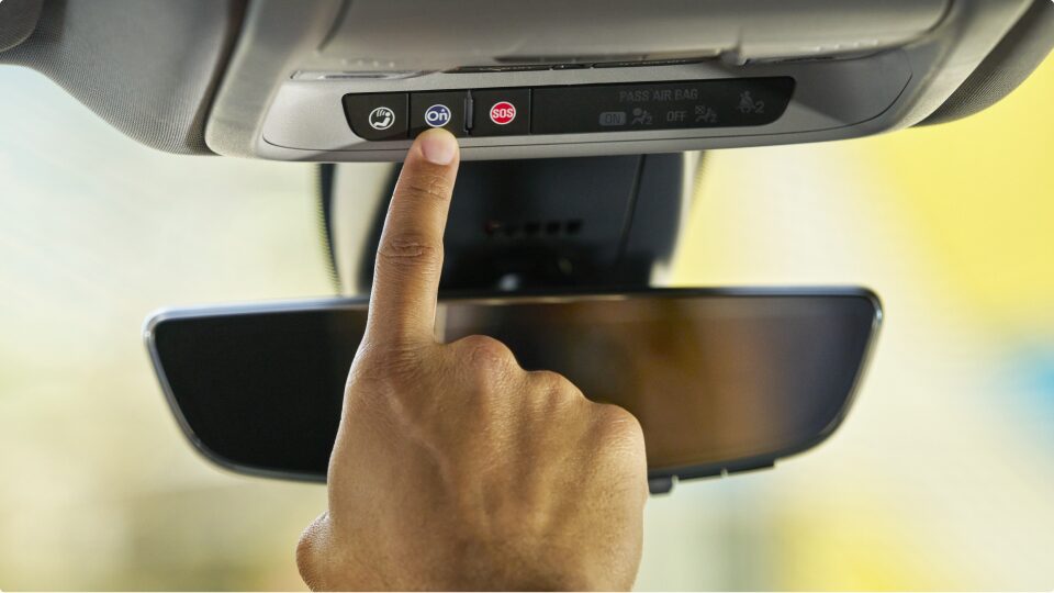 Primer plano de una mano presionado el botón OnStar dentro de un vehículo Chevrolet.