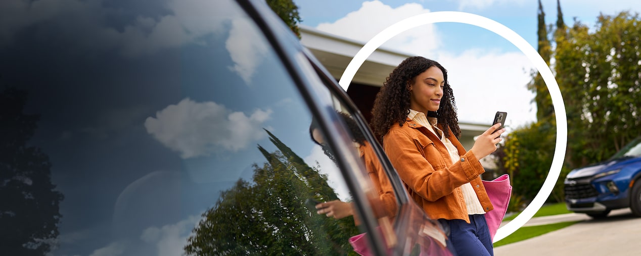 Imagen de una mujer usando su celular junto a su auto estacionado frente a una casa, mientras se destaca el mensaje: OnStar, tecnología que te cuida a vos. 