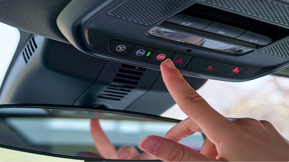 Primer plano de una mano presionado el botón OnStar dentro de un vehículo Chevrolet.