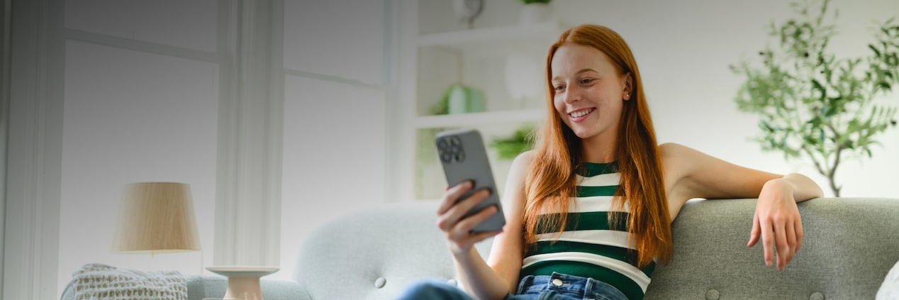 Persona sentada en un sofá utilizando un teléfono móvil para consultar información sobre un plan desde su hogar.