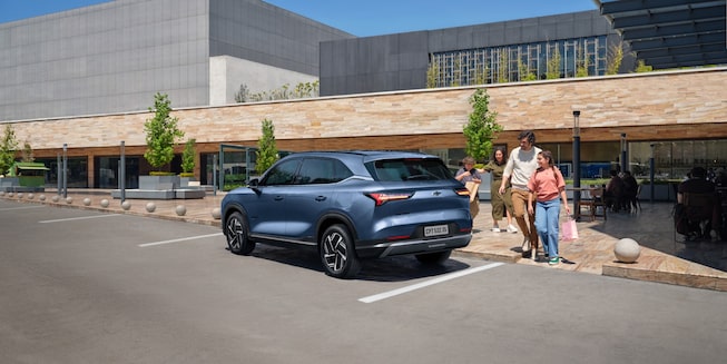Chevrolet Captiva PHEV estacionada en la puerta de un local comercial mientras una familia se aproxima a ella para guardar bolsas de compras.