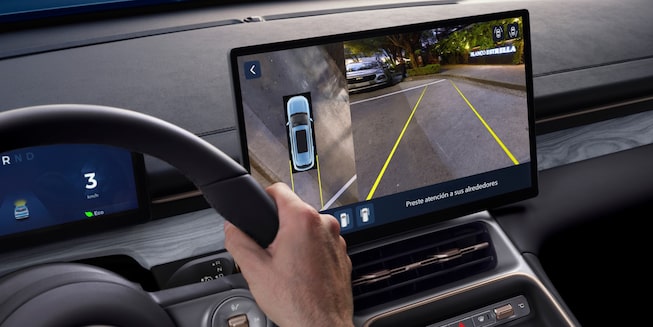 Imagen desde el punto de vista del conductor mientras observa la pantalla central digital y estaciona con la asistencia de la cámara trasera.