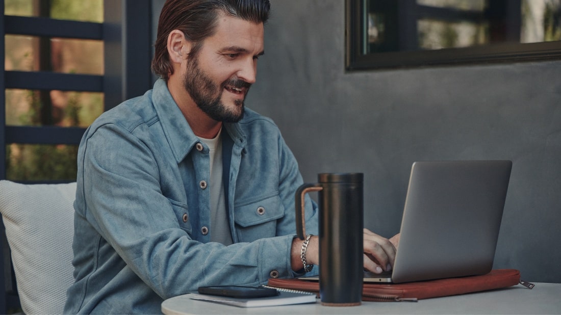 Persona sentada en una mesa con portátil, smartphone y taza, revisando información junto al texto 'Solicitud de adhesión', imagen que representa el contrato de adhesión dentro de la sección Condiciones Generales de la suscripción digital Chevrolet.