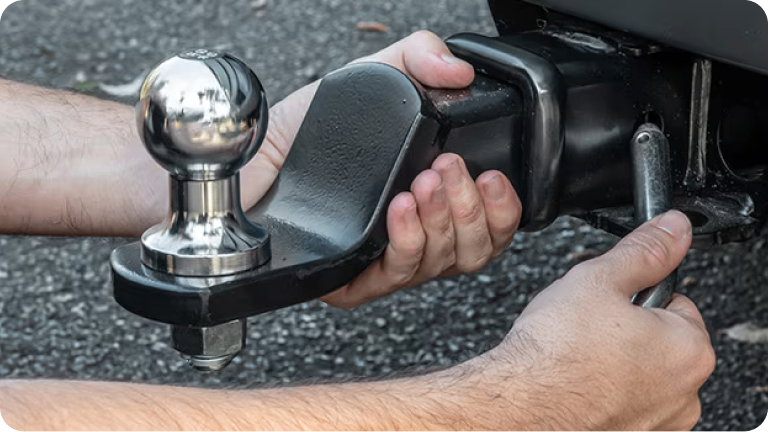 Imagen de las manos de un hombre instalando el enganche de remolque a una Schevolet Silverado. 
