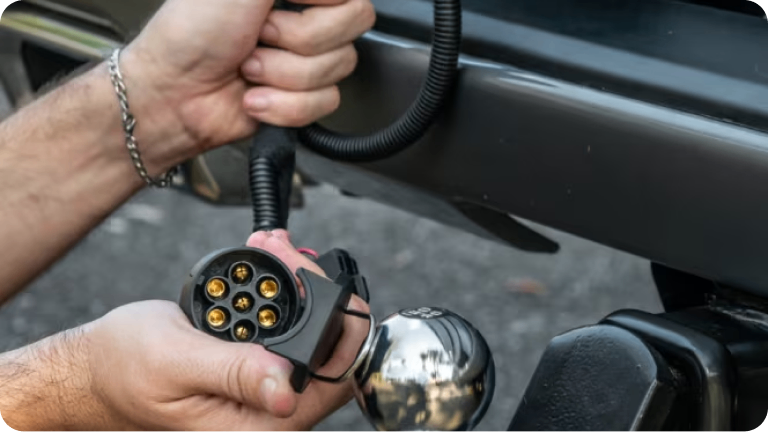 Imagen de las manos de un hombre sujetando el kit adaptador de enchufe para remolque. 
