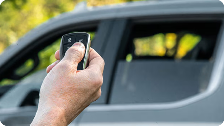 Imagen de una mano accionando el control remoto para subir los vidrios de la nueva Chevrolet Silverado, visible al fondo de la foto.