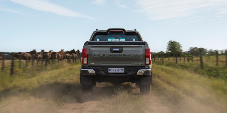 Chevrolet S10 2027 gris vista trasera conduciendo por un camino rural con caballos de fondo en Argentina