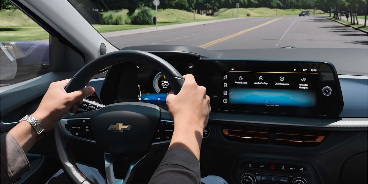 Interior de Chevrolet Onix Plus con conductor al volante, sistema de proyección inalámbrica y tablero digital de 3,5 pulgadas, mostrando funciones de conectividad y monitoreo de conducción.