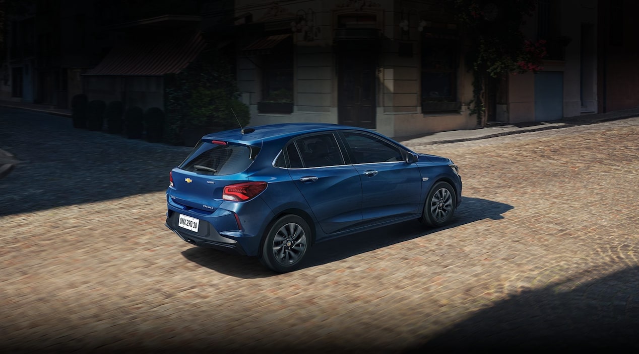Chevrolet Onix LT Turbo MT azul circulando por una calle adoquinada en un entorno urbano. Imagen promocional de Plan Chevrolet con información de financiación de hasta 80% en 120 cuotas y seguro bonificado al 50% durante los primeros 3 meses.