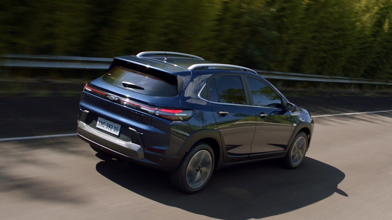Vista trasera del Chevrolet Sonic circulando por una ruta con un bosque de fondo.