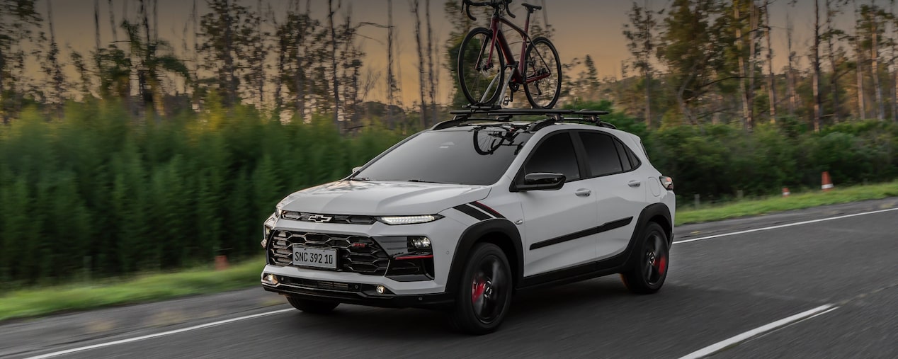 Chevrolet Sonic circulando por una ruta equipado con un porta bicicleta con vegetación de fondo.