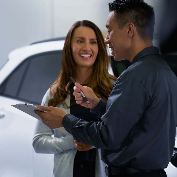Un asesor de ventas Chevrolet sostiene una carpeta con papeles y una lapicera mientras conversa con una clienta.