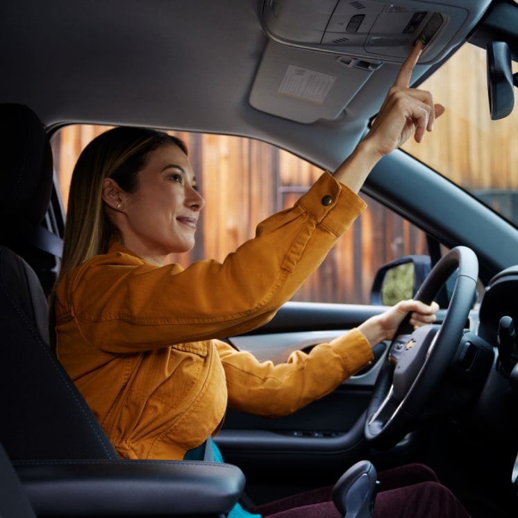 Una mujer manejando un vehículo Chevrolet mientras presiona el botón de OnStar en el panel.