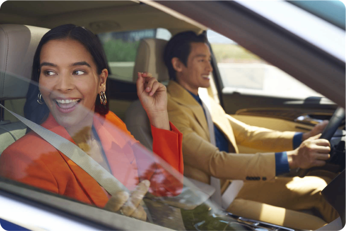 Una pareja dentro de un vehículo Chevrolet: la mujer, en el asiento del acompañante, sonríe mientras mira hacia afuera; el hombre también sonríe mientras maneja.