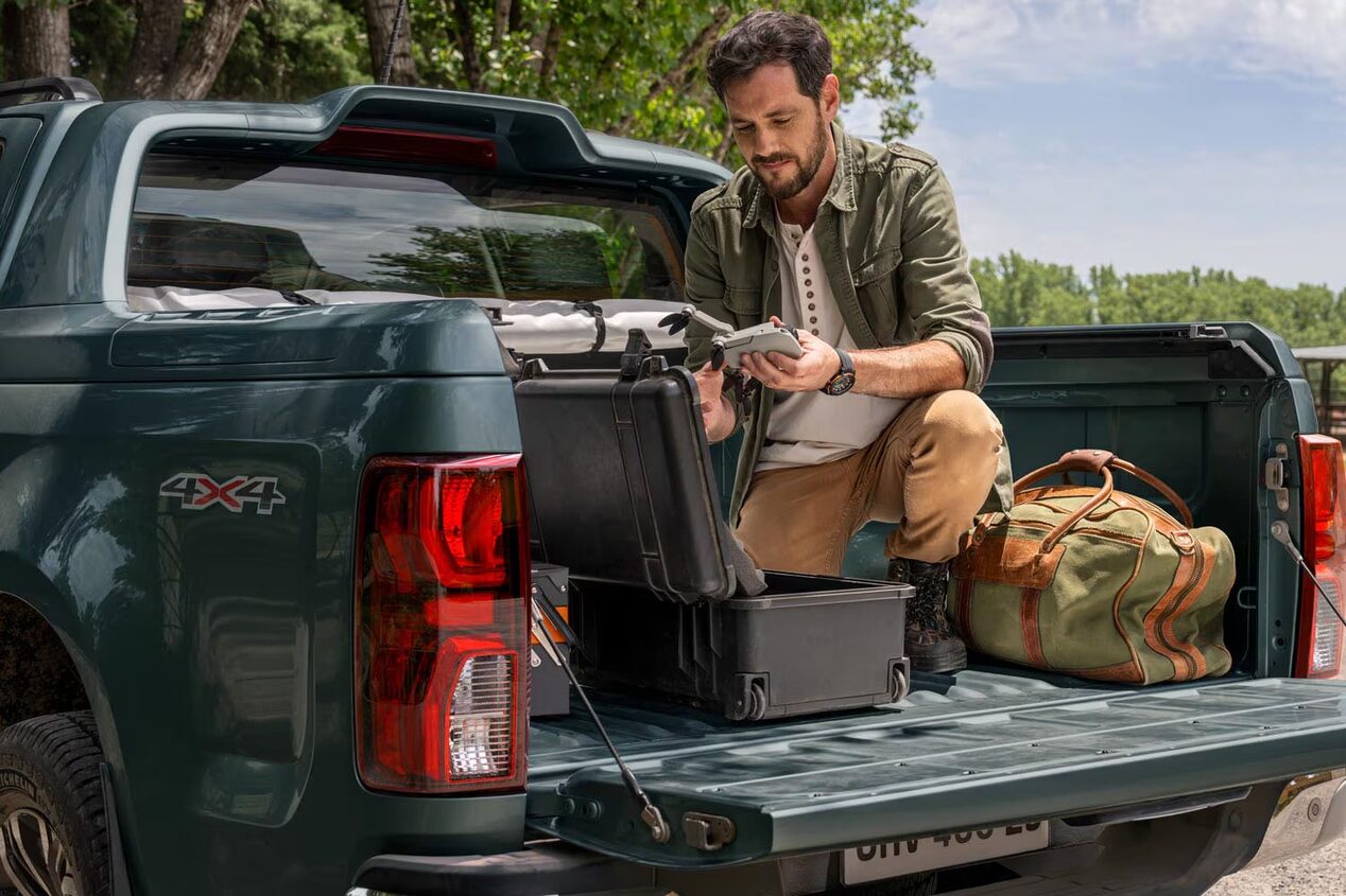 Imagen de un hombre subido y agachado en la caja de una Chevrolet Colorado mientras arma un dron.