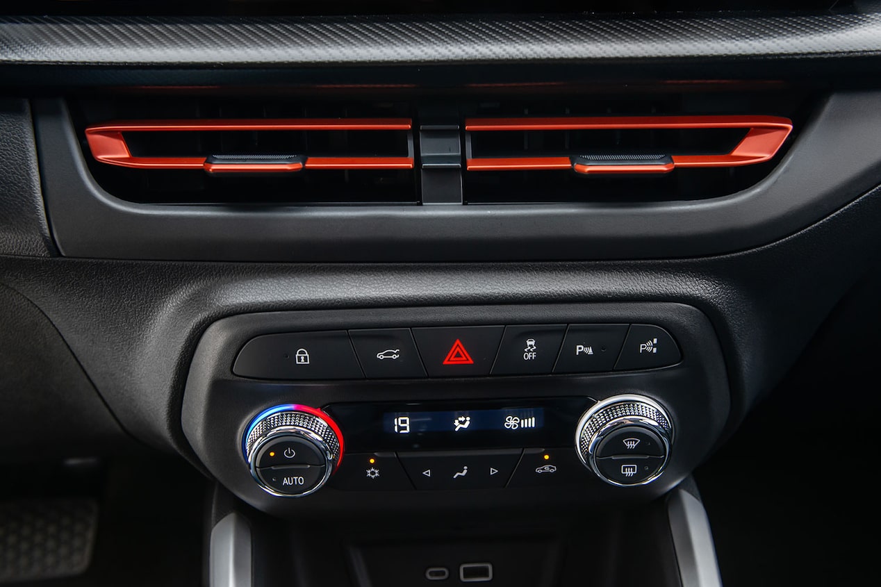 Panel central del Chevrolet Onix Sedán con aire acondicionado digital y control de temperatura, mostrando perillas iluminadas, pantalla de climatización y detalles en color rojo en las rejillas de ventilación.