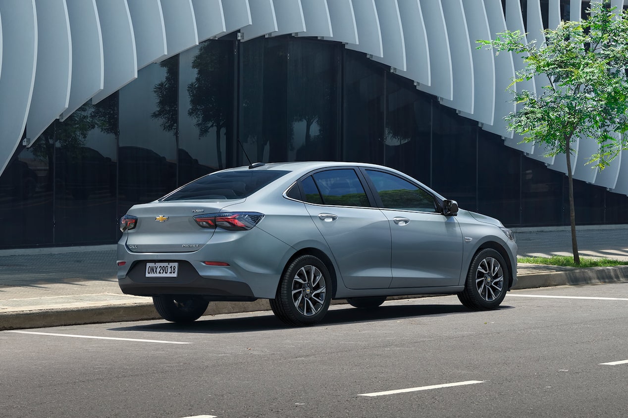 Chevrolet Onix Sedán estacionado en paralelo sobre una calle urbana, destacando el uso del asistente de parqueo semi-automático y su diseño moderno visto desde la parte trasera.