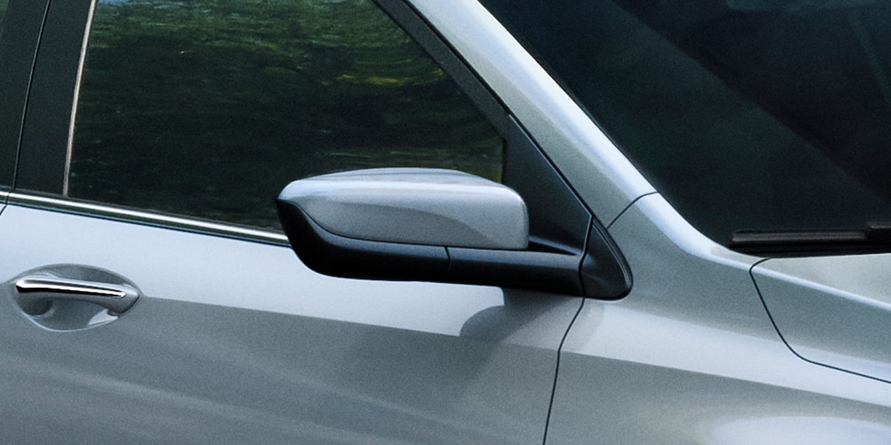 Espejo lateral del Chevrolet Onix Sedán, con diseño aerodinámico y acabado en negro brillante en la base, visto en detalle desde el costado del vehículo.