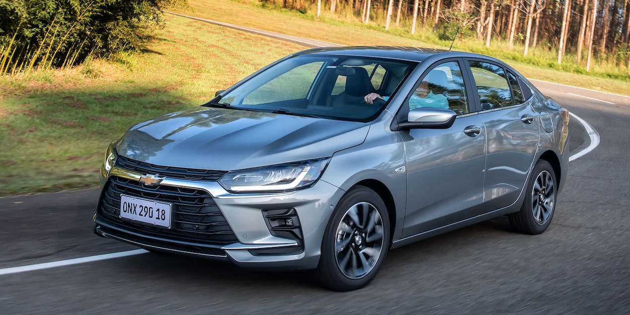 Chevrolet Onix Sedán circulando por una carretera rodeada de árboles.