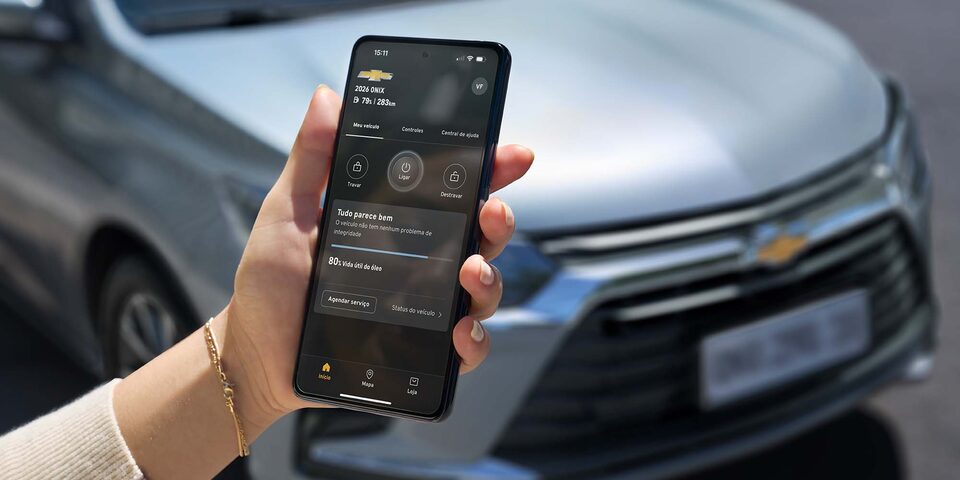 Persona sosteniendo un smartphone con la aplicación de myChevrolet conectada al Onix Sedán, mostrando en pantalla funciones de control remoto y diagnóstico del vehículo, con el auto visible al fondo.