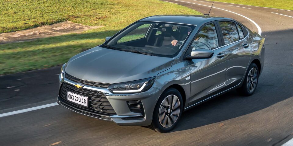 Chevrolet Onix Sedán circulando por una carretera rodeada de árboles.
