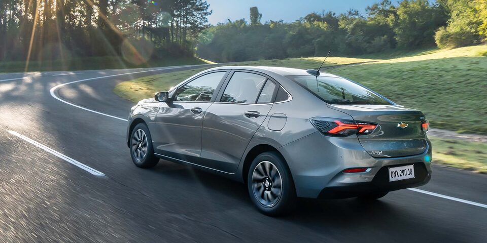 Chevrolet Onix Sedán circulando por una carretera rodeada de árboles, visto desde atrás.