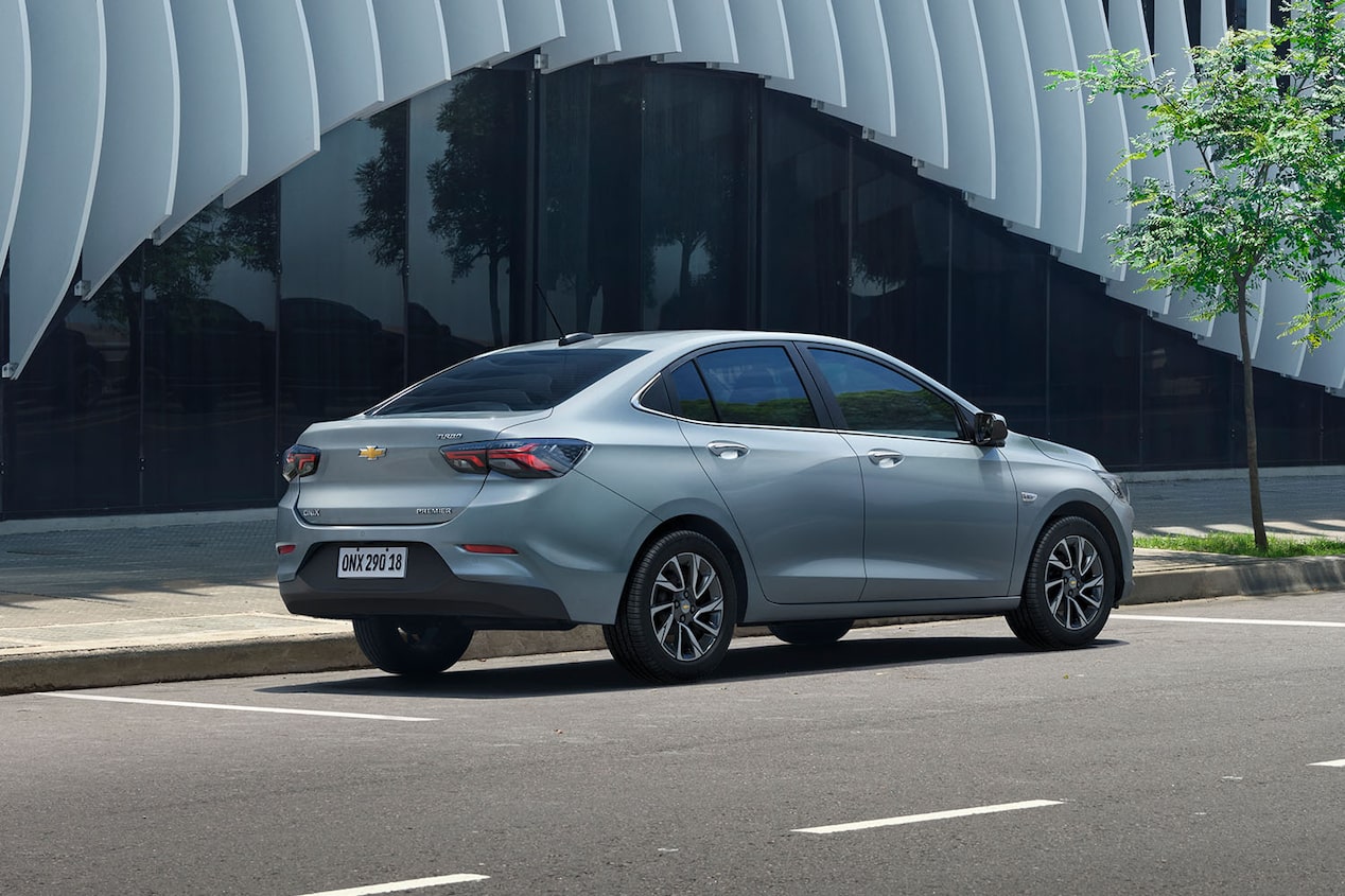 Chevrolet Onix Sedán estacionado en paralelo sobre una calle urbana, destacando el uso del asistente de parqueo semi-automático y su diseño moderno visto desde la parte trasera.