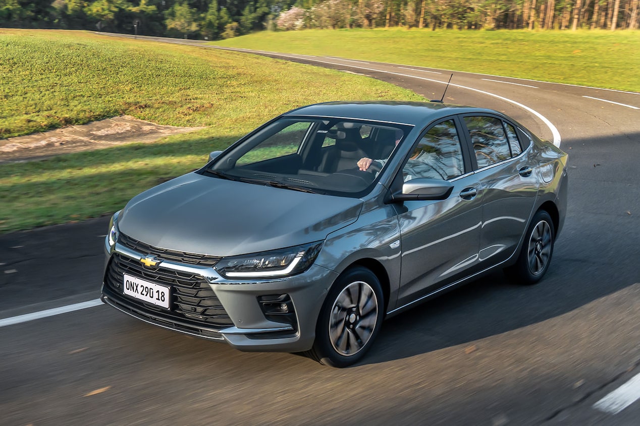 Chevrolet Onix Sedán circulando por una carretera rodeada de árboles.