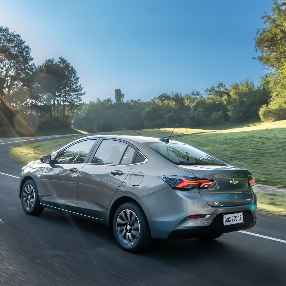Chevrolet Onix Sedán circulando por una carretera rodeada de árboles, visto desde atrás.