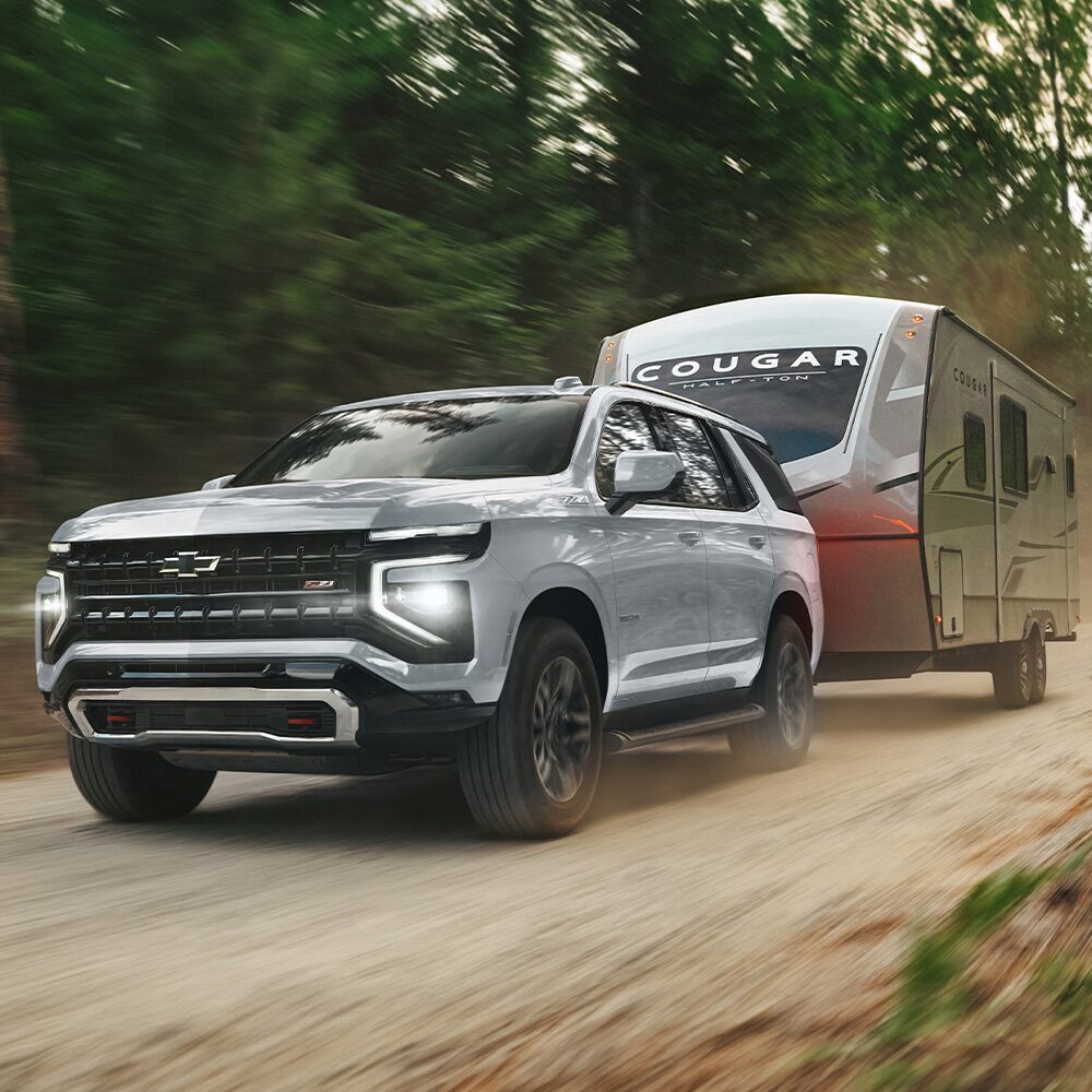 Chevrolet Tahoe transportando un tráiler por un camino de tierra con vegetación de fondo.