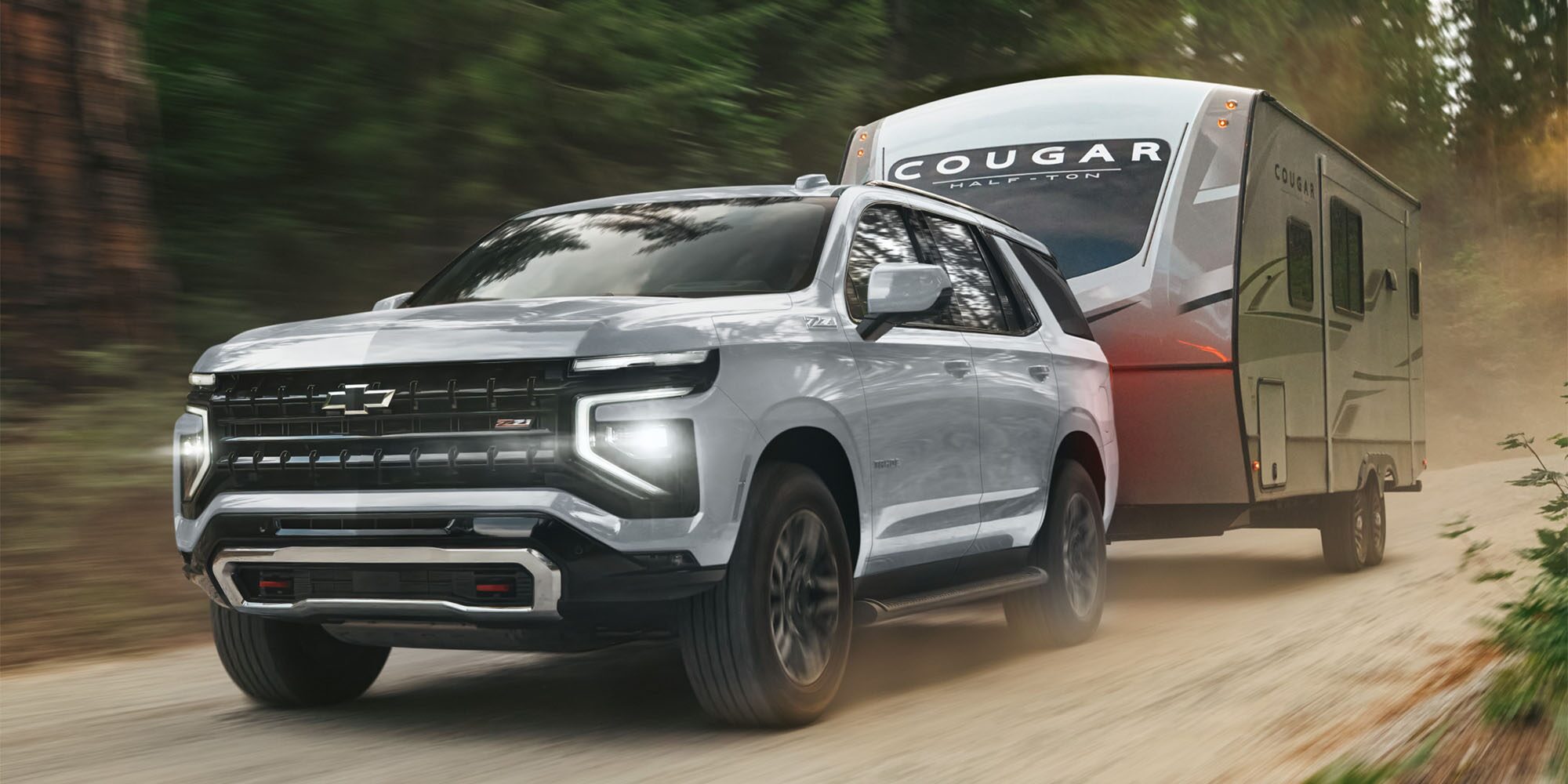 Chevrolet Tahoe transportando un tráiler por un camino de tierra por un bosque.