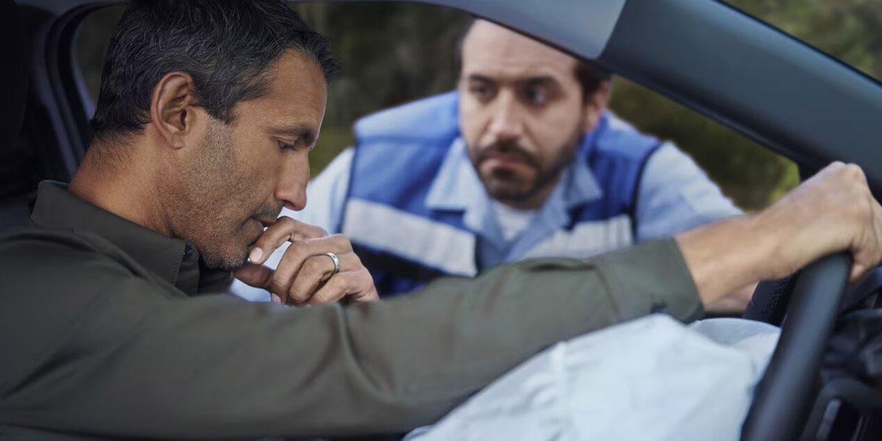 Conductor dentro de un auto tras un accidente, con el airbag desplegado, mientras un operador de asistencia lo acompaña desde la ventanilla.